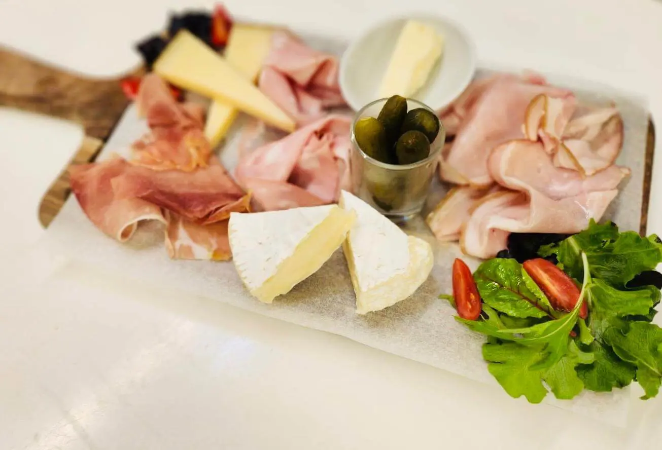 A beautifully arranged charcuterie board with assorted cheeses, slices of prosciutto and cucumbers.